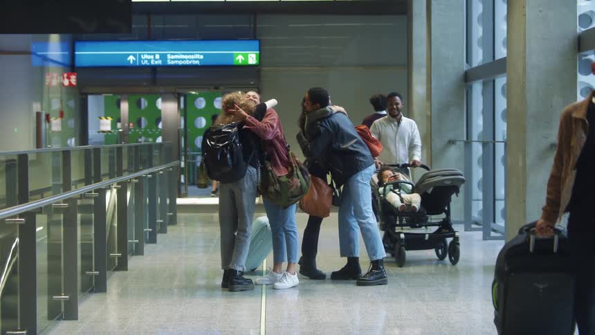 A group of female friends with leather jacket jeans luggage and backpack cuddles each other at the airport