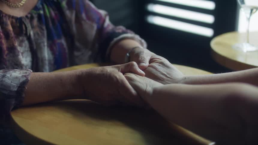 A woman in a room holding another woman hand over a table
