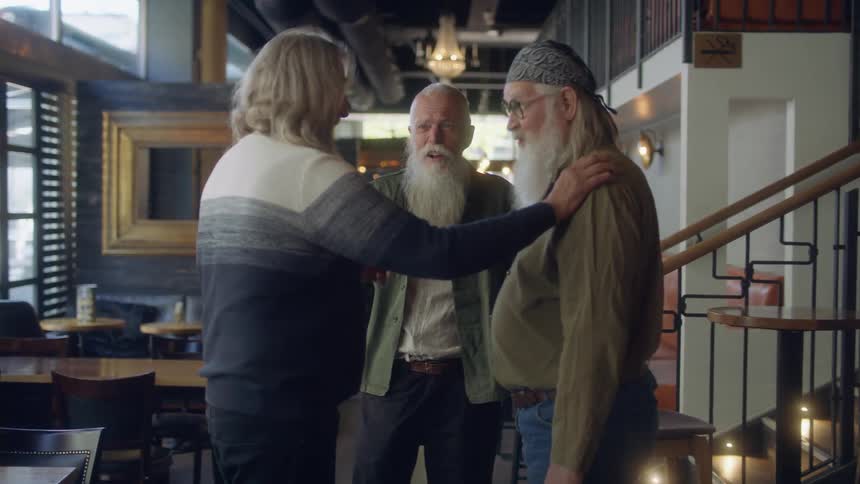 A man puts his hand on another mans shoulder as they stand in a restaurant