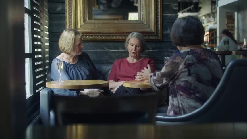 Elderly women sit at a table in a bar as employees work in the background