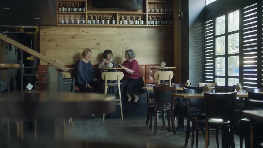 Middle aged women sit at table and talk to each other in cafe