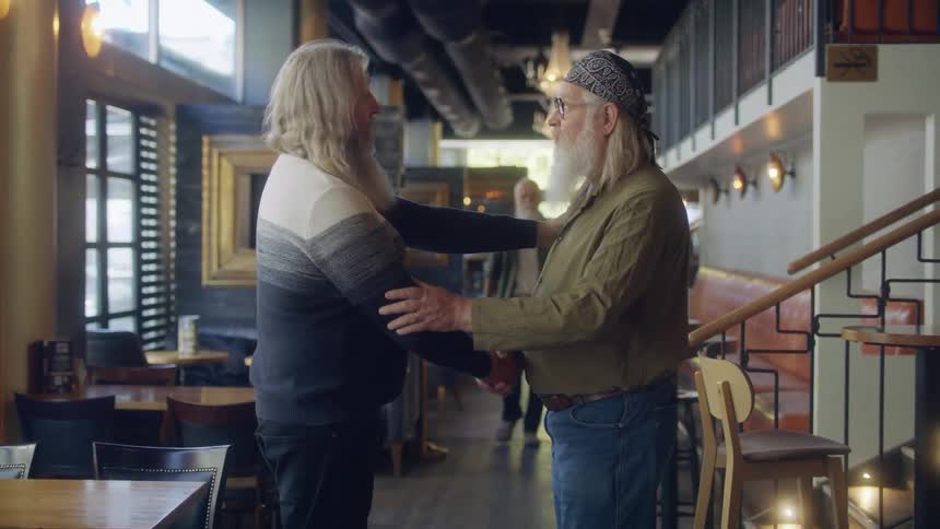 A pair of graying men greet each other with a handshake in a restaurant
