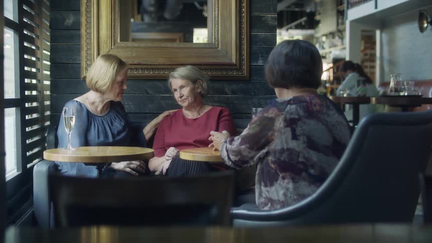 Three mature women are sitting in a restaurant in the daytime comforting one of them that is depressed