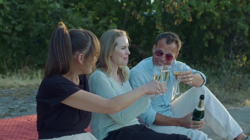 A man pours drinks and they toast outside