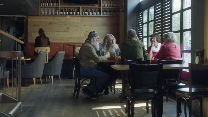 Group of elderly friends sitting at a table in a bar talking