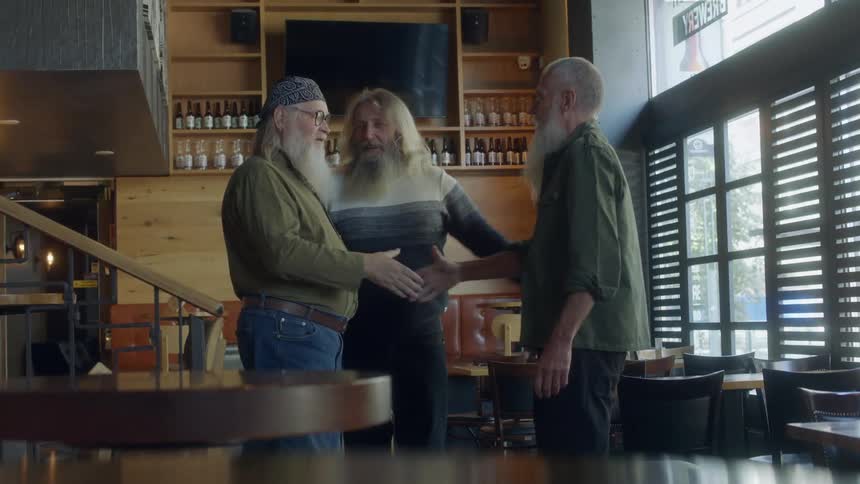 Three older men greet each other by shaking hands
