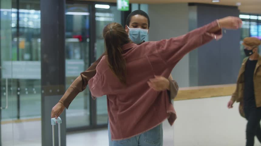 Friends wearing face masks greet each other with a hug on a passenger terminal