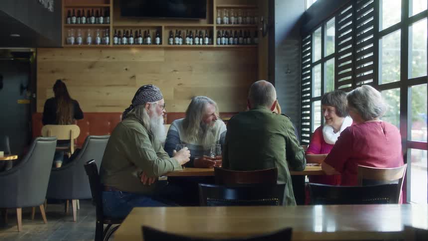 A group of older men and women sit together while talking and laughing over a few glasses of beer