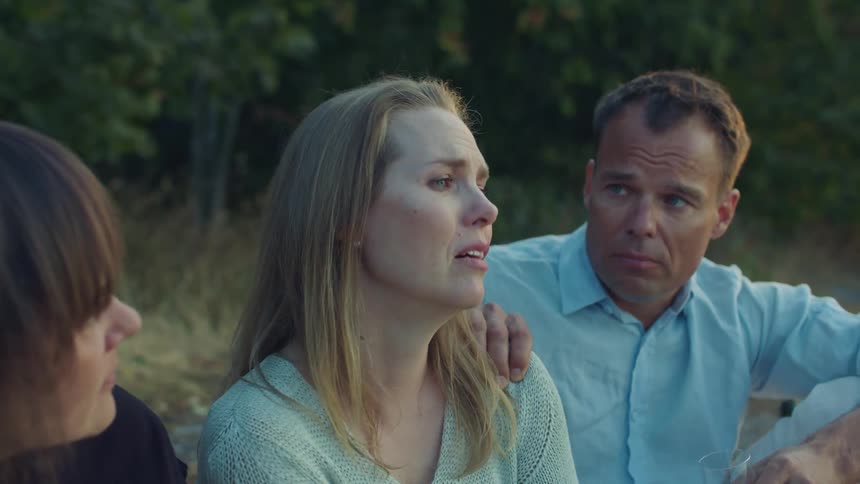 Three friends sit on ground with wine glass two comforting a woman as she tears up