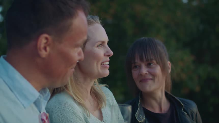 Three friends are having wine while standing outdoors talking and laughing at dusk