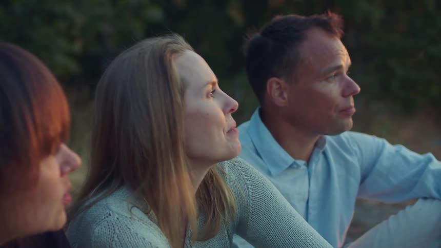 Friends sitting outdoors at sunset drinking champagne while talking