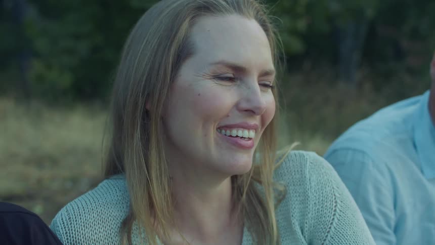 Friends sit on ground laughing with woods in background