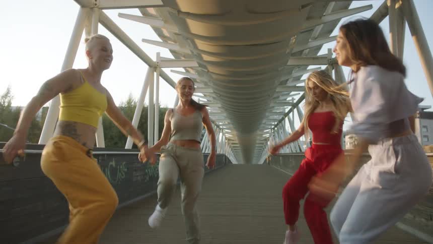 Four young women perform a choreographed dance on a pedestrian bridge