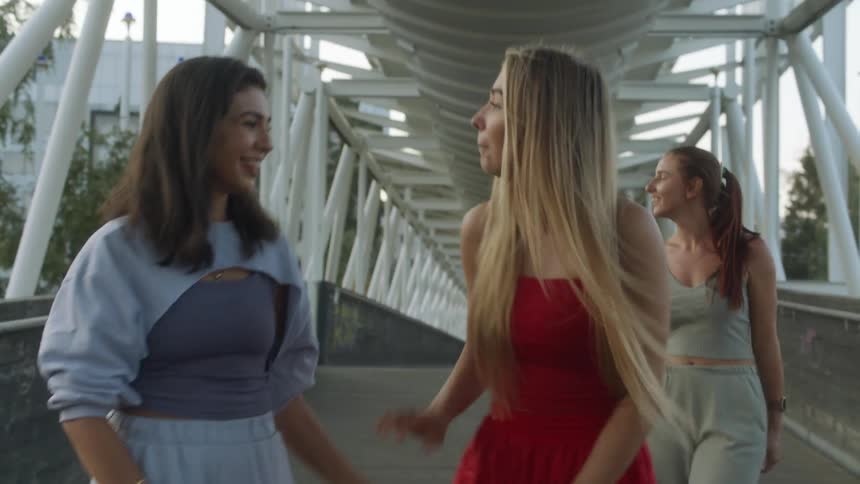 Four girl friends laugh and horse around as they walk on a pedestrian bridge