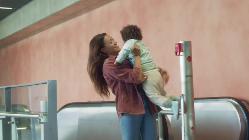 Woman carrying luggage out an escalator greets her family on a passenger terminal