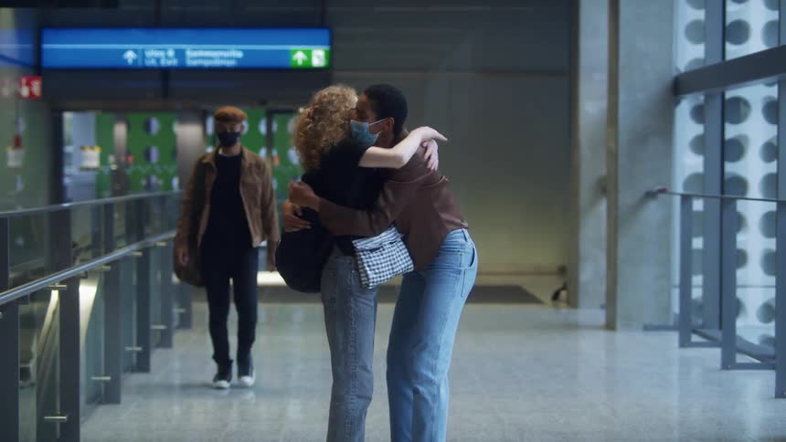 Women hug as they meet at terminal walking along arm in arm