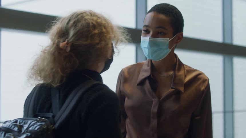 Friends wearing face masks greet each other in a passenger terminal