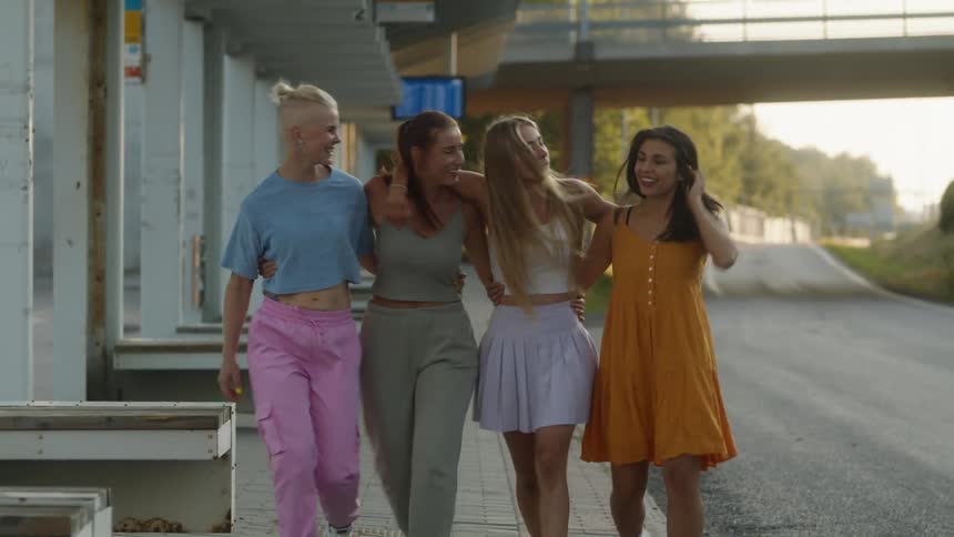 Four women walk on the sidewalk arm in arm