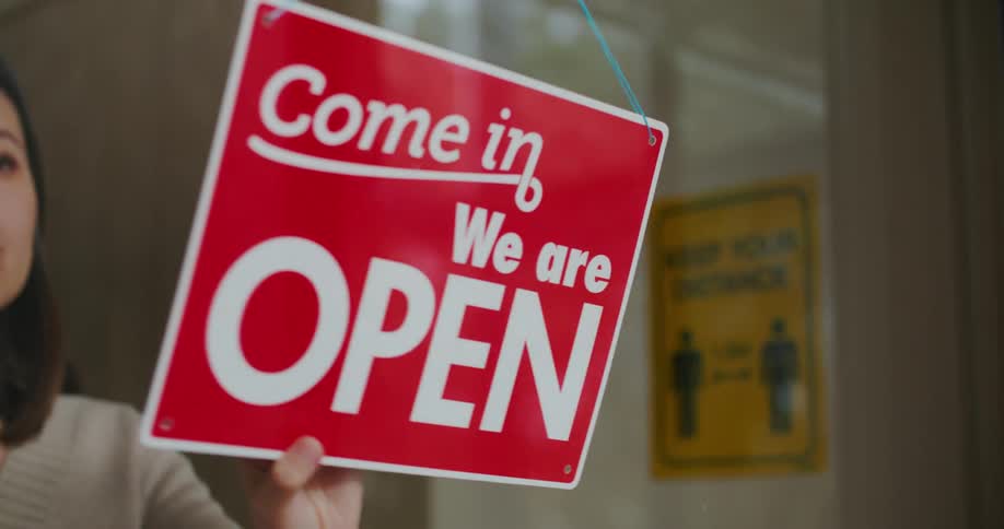 An employee flipping a closed sign to open at a shop
