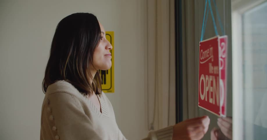 A shopkeeper flips the stores open sign to indicate the store being closed during the day