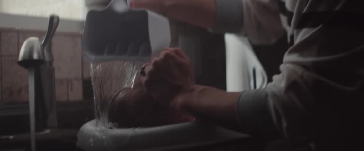 A mother bathing her newborn in a kitchen sink at home