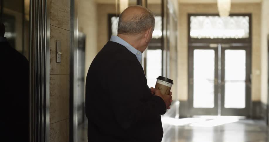 Elderly man holding a cup of coffee on the hallway of a building loby