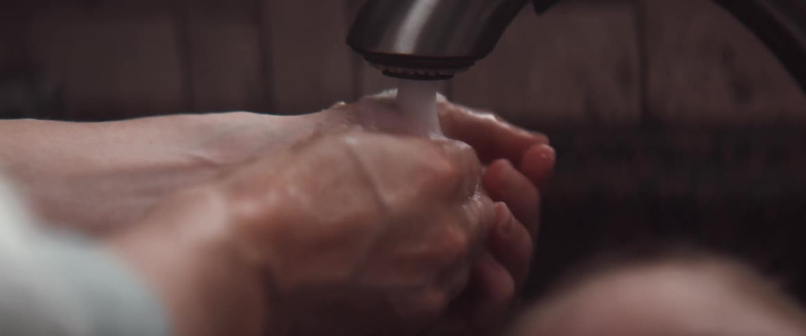 Woman washes hands under faucet next to baby