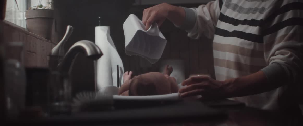 A woman giving a baby a bath by a sink with water coming out of the faucet