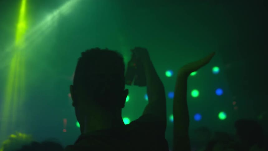 Silhouette of a man holding bottles of beer walking through a dancing crowd in a night club