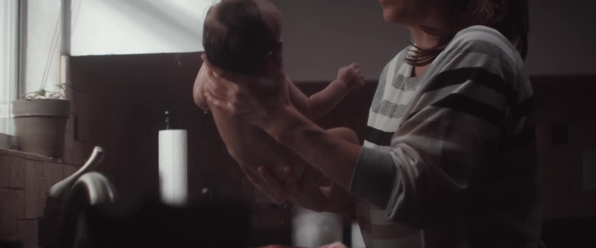 A mother finishes bathing a baby in a kitchen sink