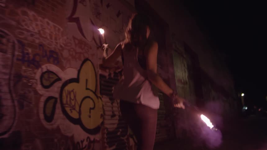 Young woman holding flares dances on the city street at night