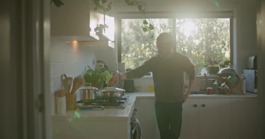 A man puts his cellphone away to check on food cooking on the stove