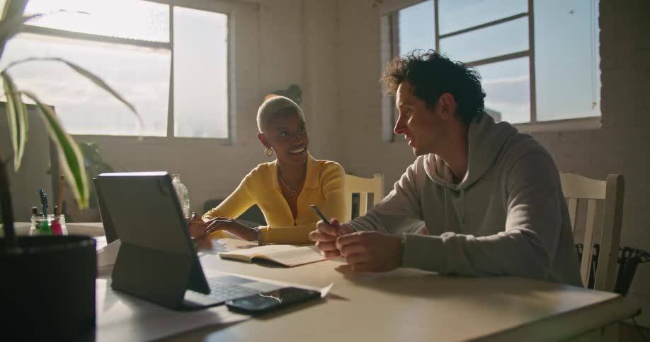 Woman with short hair hoop earrings and yellow sweater and man in gray hoodie work on laptop