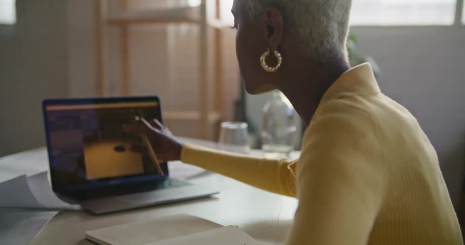 A woman talking while taking notes and using a laptop