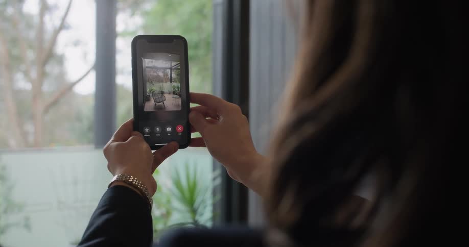 Woman wearing suit talks to man via video call before filming backyard from inside room