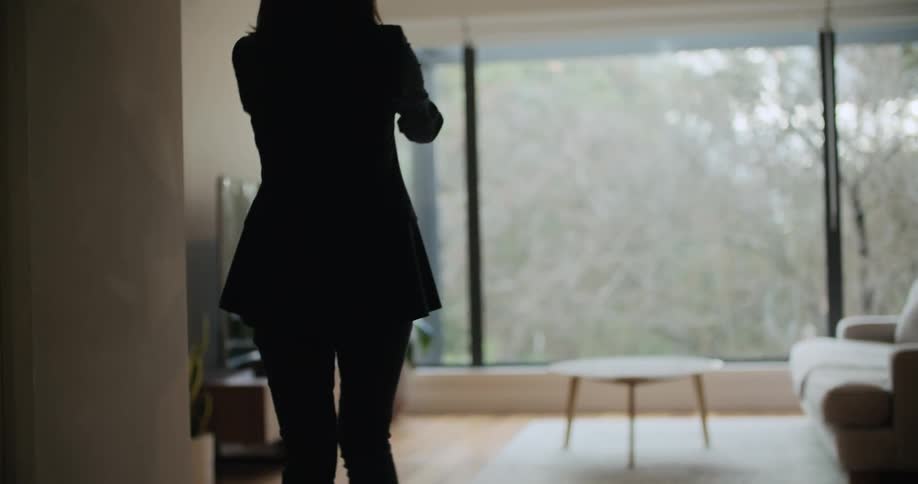 A woman walks around a house while filming the interior with her smartphone