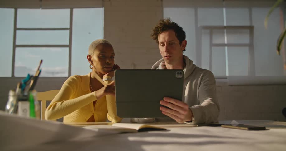 A man and woman talk while looking at a tablet