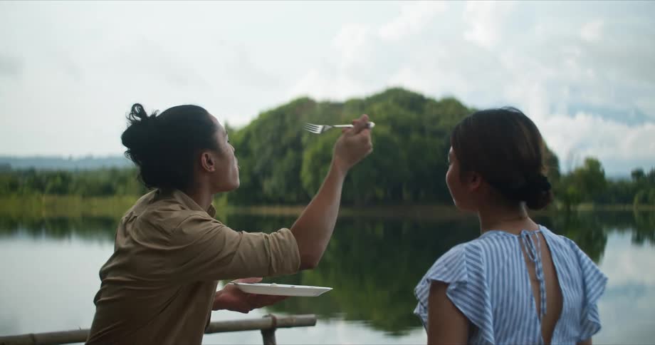 Young couple playfully eating food while sitting near a lake
