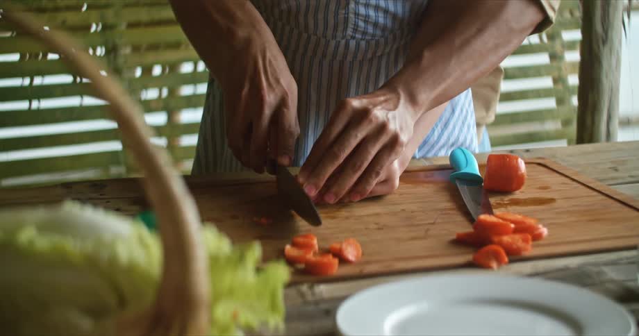 A man stands behind a woman and with hands guiding hers slices through a carrot before they look at each other and laugh