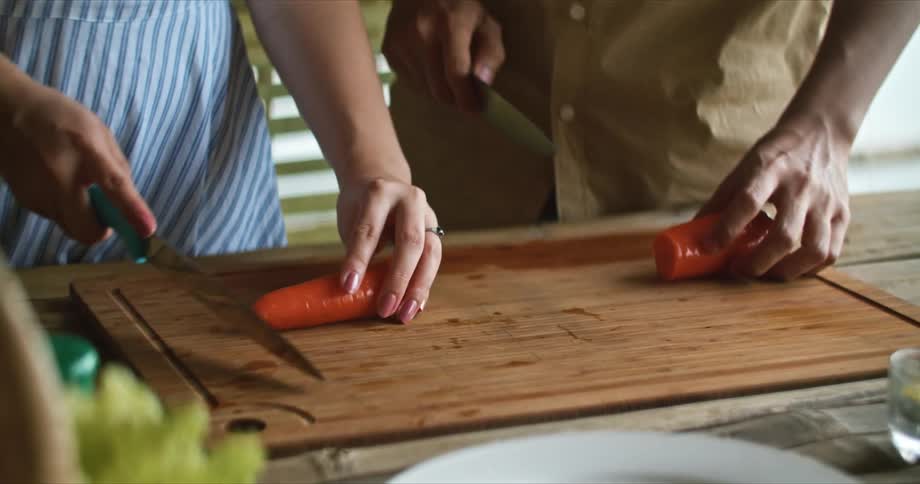 Man and woman slice carrots on wooden chopping board together