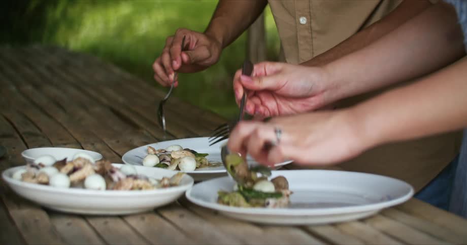 A woman adds food to her plate standing next to a man at a wooden table