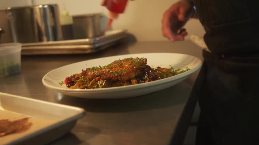 Chef seasoning a dish over the countertop on the kitchen of a restaurant