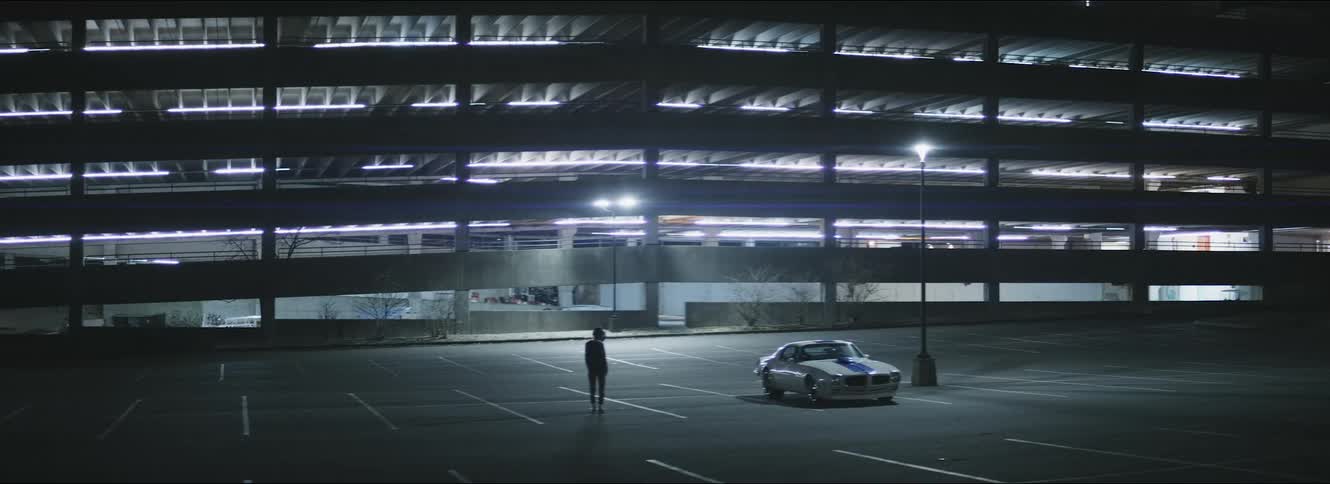 A person standing in a parking lot in front of a parking garage walks towards a car