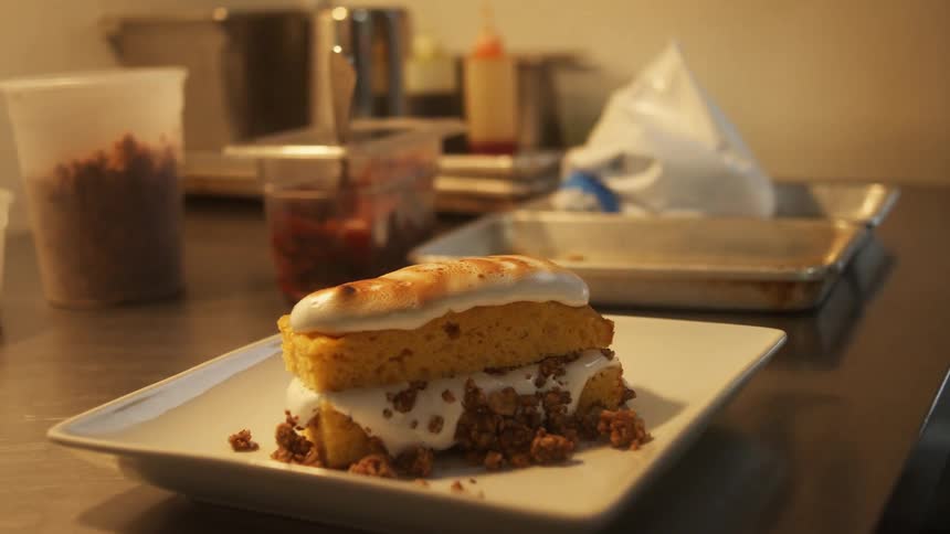 A chef torching a dessert on a white platter in a restaurant kitchen
