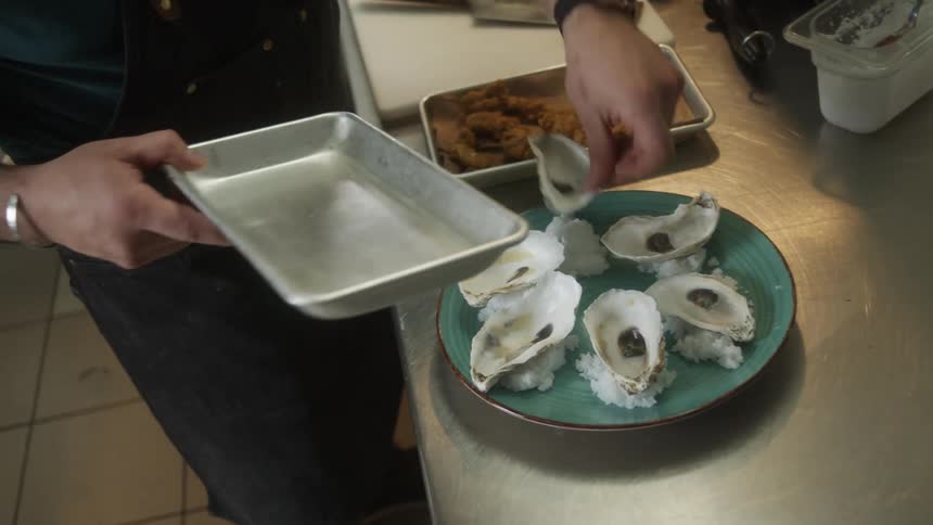 A person adding oyster shells on top of rice on a plate