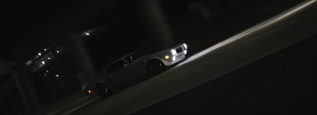 A sports car is driving on a street at night with its lights on