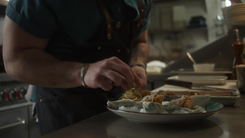 A male chef adding garnish to a plate of food in a restaurant kitchen
