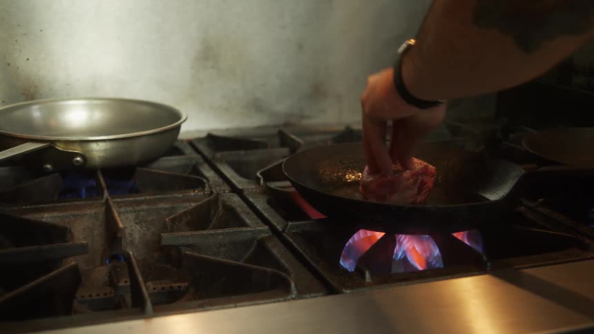 A chef picks up a filet and places it in a hot cast iron pan pressing down a bit
