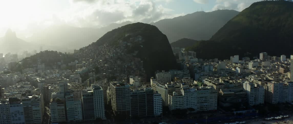 Mist hovers over city sitting between water beach and tall mountains and encircling smaller mounds