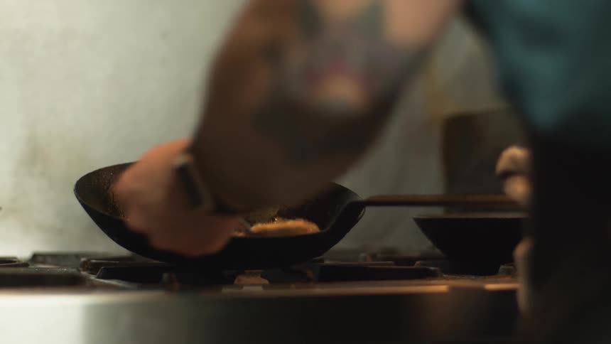 A chef holds a tilted cast iron pan spooning sauce over a repeatedly over a steak